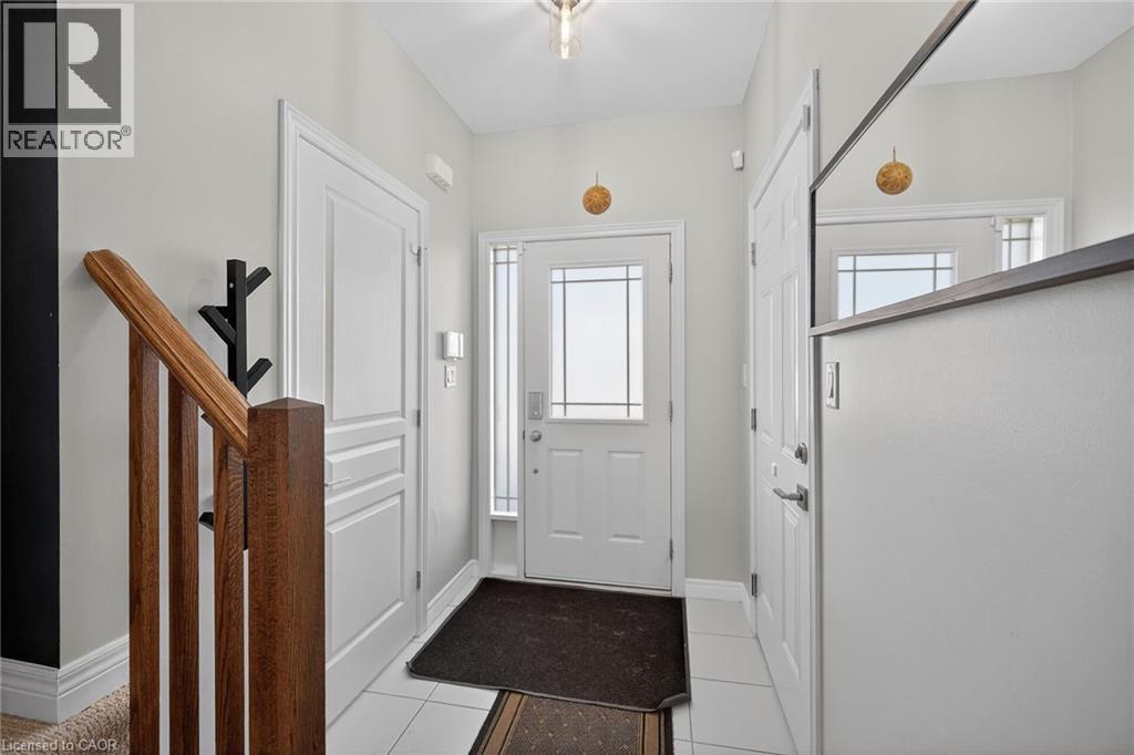 Entryway featuring a white paneled door with sidelights, white tile flooring, and a wood-finish staircase with square balusters - 149 Kinsman Drive, Binbrook, ON
