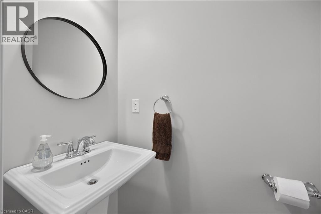 Pedestal sink with chrome fixtures and an oval black-framed mirror - 149 Kinsman Drive, Binbrook, ON