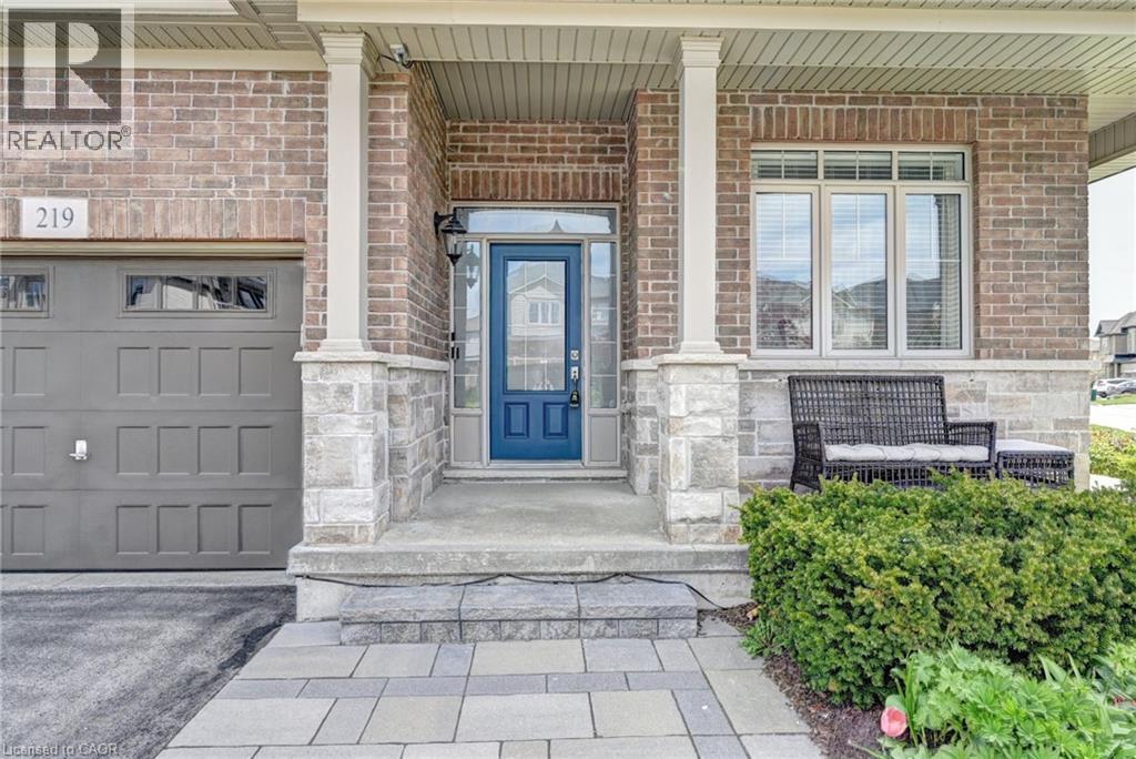 Brick and stone facade featuring a prominent blue entry door, an integrated garage with transom windows, and a covered porch with architectural columns - 219 Falconridge Drive, Kitchener, ON - Outdoor