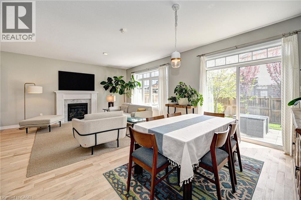 Bright open-concept living and dining area featuring wood-finish flooring, a white mantel fireplace, and a sliding glass door to the patio - 219 Falconridge Drive, Kitchener, ON - Indoor With Fireplace