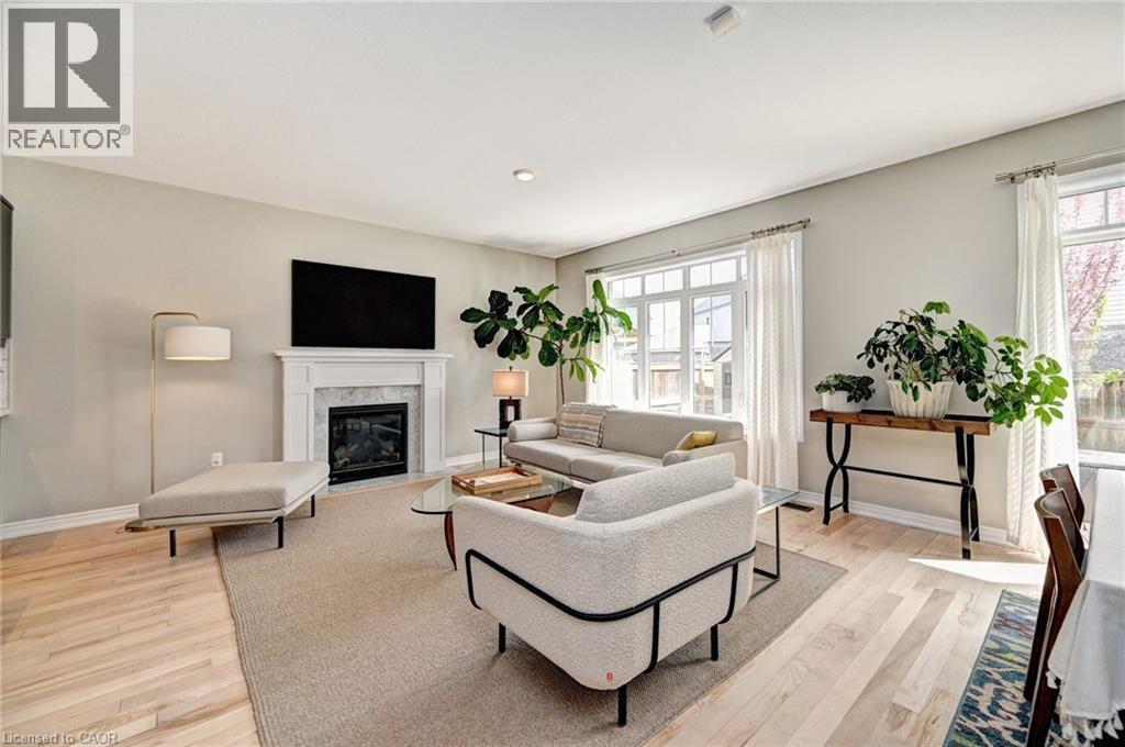 Living area featuring light wood-finish flooring, a white mantel fireplace with a dark stone surround, and multiple large windows with white trim - 219 Falconridge Drive, Kitchener, ON - Indoor Photo Showing Living Room With Fireplace