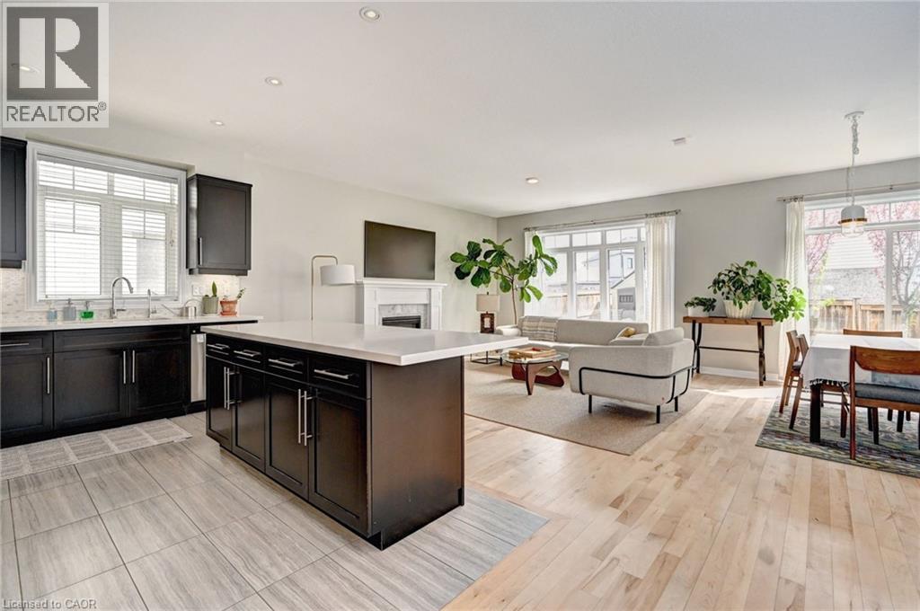 Open-concept living space featuring a kitchen island, dark wood-finish cabinetry, light wood-finish flooring, a white fireplace with mantle, and white window blinds - 219 Falconridge Drive, Kitchener, ON - Indoor