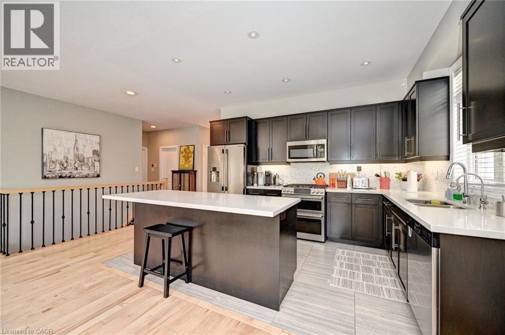 Modern kitchen featuring dark wood-finish cabinetry, stainless steel appliances, white countertops, and a full tile backsplash - 219 Falconridge Drive, Kitchener, ON - Indoor Photo Showing Kitchen With Upgraded Kitchen