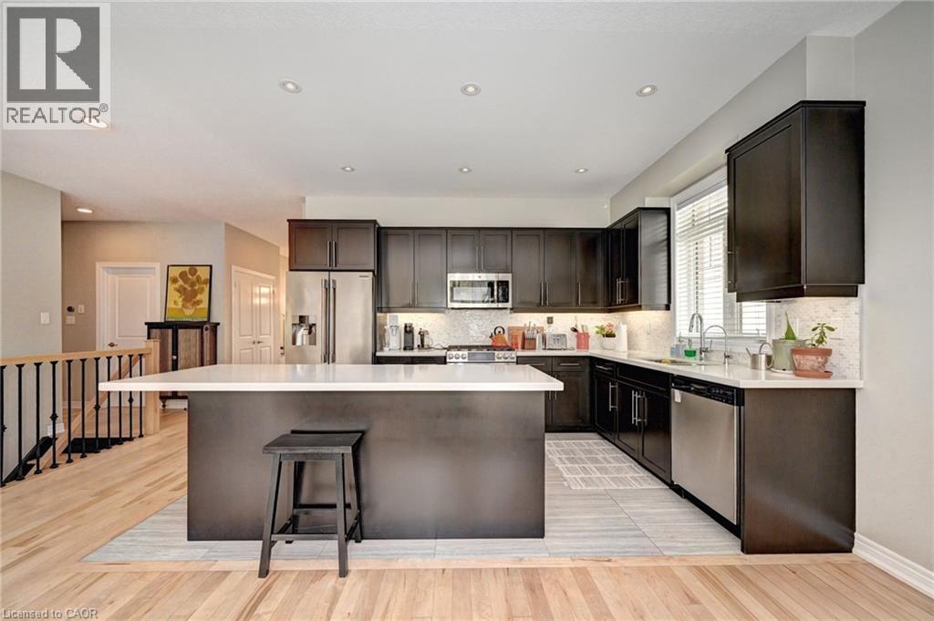 Modern kitchen featuring dark wood cabinetry, stainless steel appliances, a white solid surface countertop, and a center island with bar seating - 219 Falconridge Drive, Kitchener, ON - Indoor Photo Showing Kitchen With Upgraded Kitchen