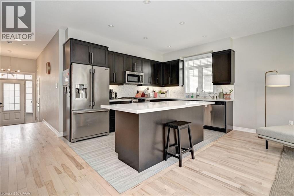 Modern kitchen with dark wood-finish cabinetry, stainless steel appliances, and a central island with a white countertop - 219 Falconridge Drive, Kitchener, ON - Indoor Photo Showing Kitchen With Upgraded Kitchen