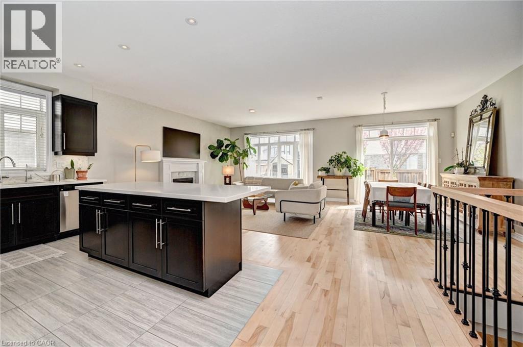Open-concept living area featuring a kitchen with dark cabinetry and white countertops, a central island with storage, light wood-finish flooring, and multiple windows providing natural light - 219 Falconridge Drive, Kitchener, ON - Indoor