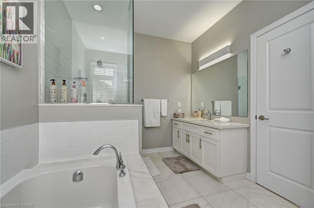Modern bathroom featuring a built-in tub with white subway tile surround, a glass-enclosed shower, a double vanity with white cabinetry, a large mirror, and neutral-toned floor tiling - 219 Falconridge Drive, Kitchener, ON - Indoor Photo Showing Bathroom