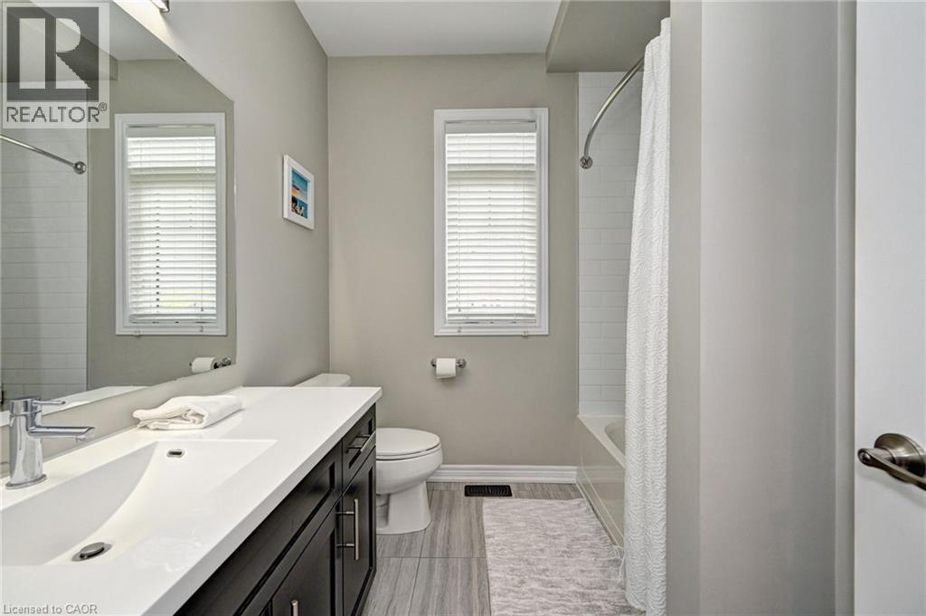 Bathroom featuring a white subway tile tub surround, dark wood-finish vanity with a white countertop, chrome faucet, and wood-finish flooring - 219 Falconridge Drive, Kitchener, ON - Indoor Photo Showing Bathroom