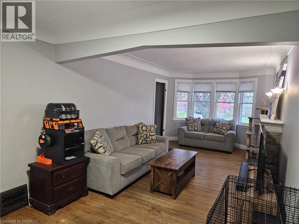 Living area featuring wood-finish flooring, a bay window with multiple panes, a stone fireplace surround, and a mantelpiece - 75 Barons Avenue S, Hamilton, ON - Indoor Photo Showing Living Room
