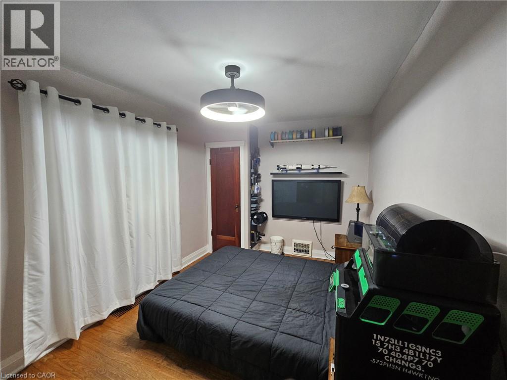 Bedroom featuring hardwood flooring, a contemporary ceiling light fixture, a wood-paneled door, and white wall-to-wall drapery - 75 Barons Avenue S, Hamilton, ON - Indoor Photo Showing Bedroom
