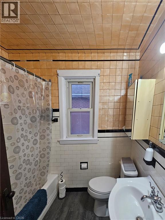 Bathroom featuring a white bathtub, toilet, and pedestal sink - 75 Barons Avenue S, Hamilton, ON - Indoor Photo Showing Bathroom