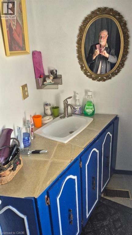 Vanity with a white ceramic sink, tile countertop, and vibrant blue cabinetry with white trim - 257 Cedar Street, Simcoe, ON - Indoor