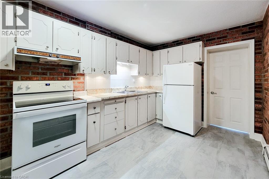 Kitchen with white appliances, brick wall, light countertops, under cabinet range hood, and light marble finish floors - 156 Park Row S, Hamilton, ON - Indoor Photo Showing Kitchen