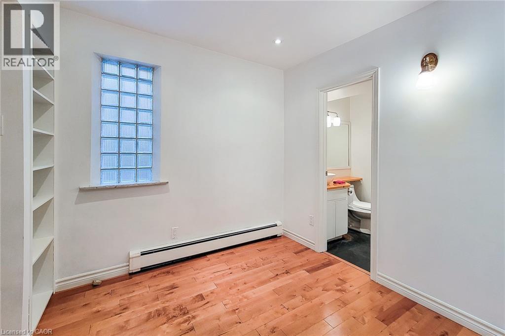 Bedroom with baseboard heating, light wood flooring, and recessed lighting. Notice the ensuite and glass block window. - 156 Park Row S, Hamilton, ON - Indoor Photo Showing Other Room