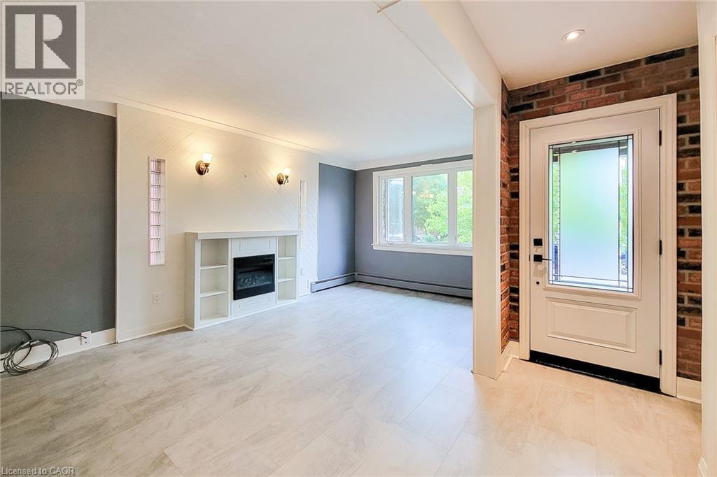 Foyer entrance with a glass covered fireplace, brick wall, and light flooring. - 156 Park Row S, Hamilton, ON - Indoor With Fireplace