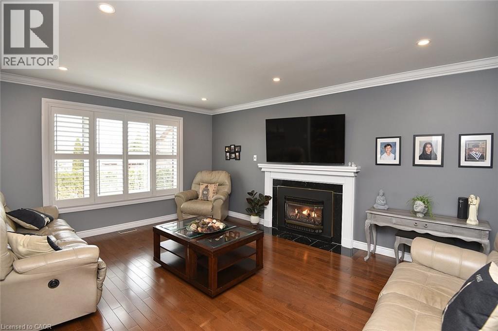 Living area featuring wood-finish flooring, a white mantel fireplace with a dark surround, and recessed lighting - 36 Tommar Place, Hamilton, ON - Indoor Photo Showing Living Room With Fireplace
