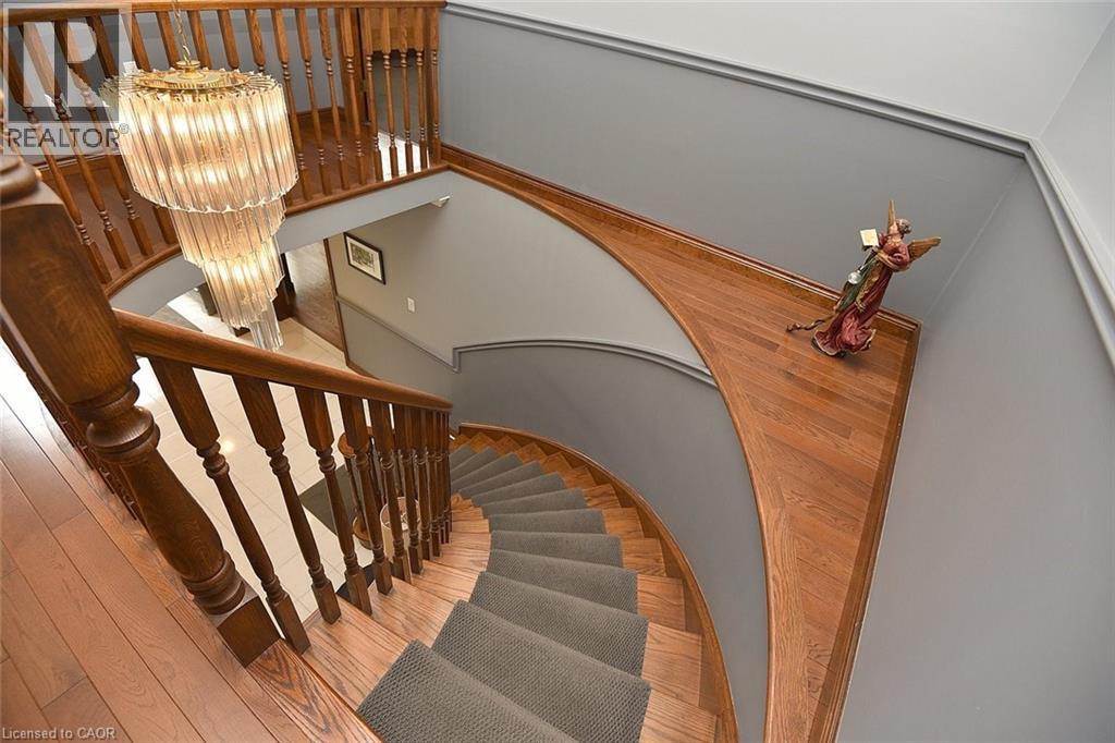 Curved hardwood staircase featuring a gray runner, wood balusters, and a tiered glass chandelier - 36 Tommar Place, Hamilton, ON - Indoor Photo Showing Other Room