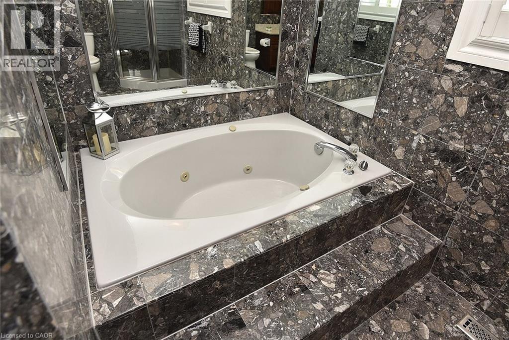 Spa-style jetted tub with polished chrome fixtures, surrounded by extensive stone-finish tiling on walls and a multi-level platform - 36 Tommar Place, Hamilton, ON - Indoor Photo Showing Bathroom