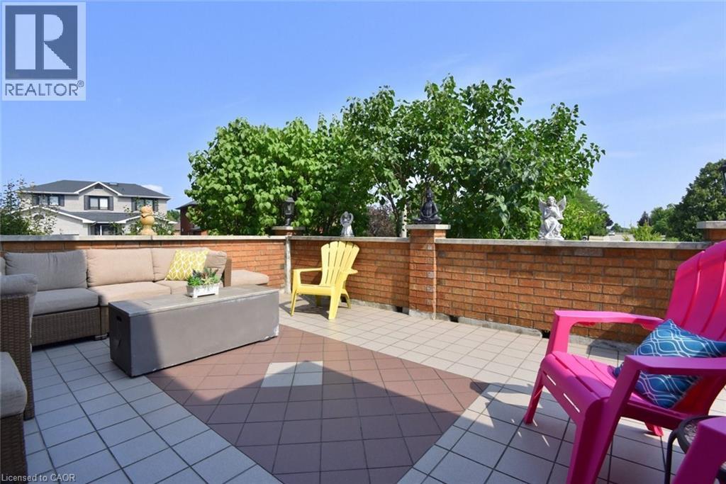Spacious outdoor patio featuring durable tile flooring, a brick half-wall, and mature tree-line perimeter - 36 Tommar Place, Hamilton, ON - Outdoor With Deck Patio Veranda