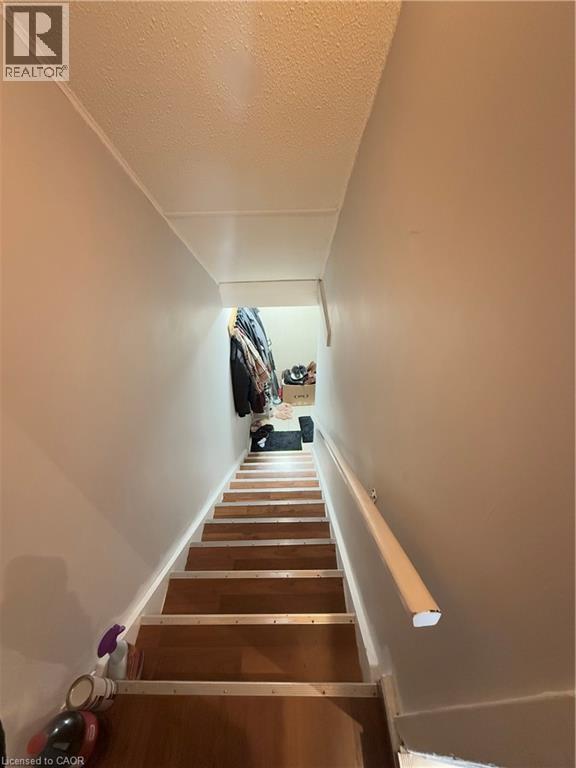 Staircase featuring wood-finish treads, light-toned risers, a wall-mounted handrail, and white painted walls - 181 Thaler Avenue, Kitchener, ON