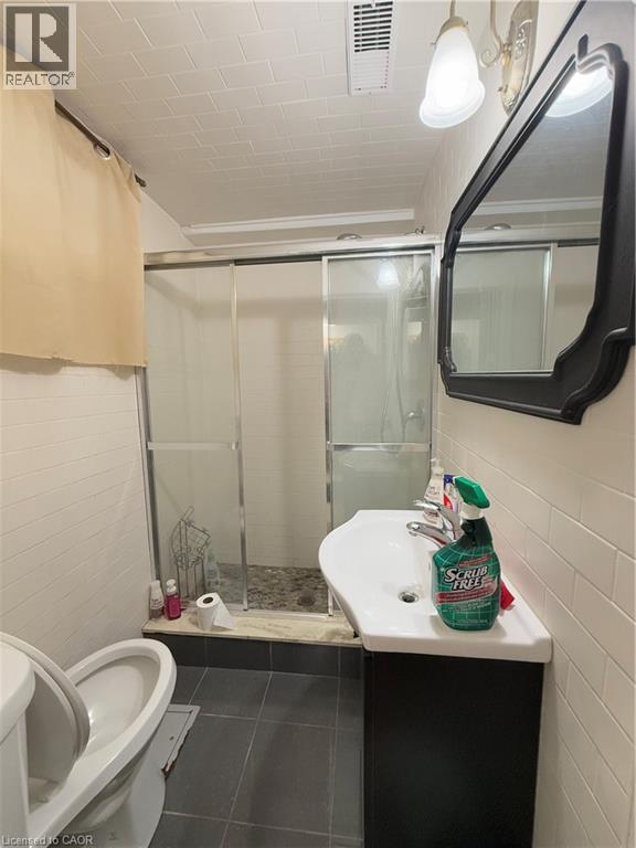 Bathroom featuring a tiled shower enclosure with sliding glass doors, a wall-mounted sink with dark cabinetry, and white subway tile walls - 181 Thaler Avenue, Kitchener, ON