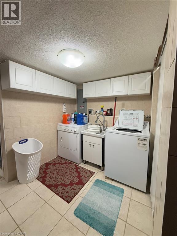 Dedicated utility room featuring tile flooring, a utility sink with cabinet storage, and extensive upper cabinetry - 181 Thaler Avenue, Kitchener, ON