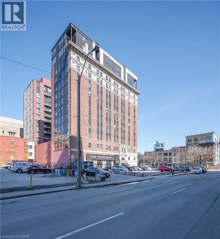 High-rise building featuring a brick facade, white architectural detailing, and a multi-level modern top section with extensive fenestration - 112 King Street E Unit# 907, Hamilton, ON