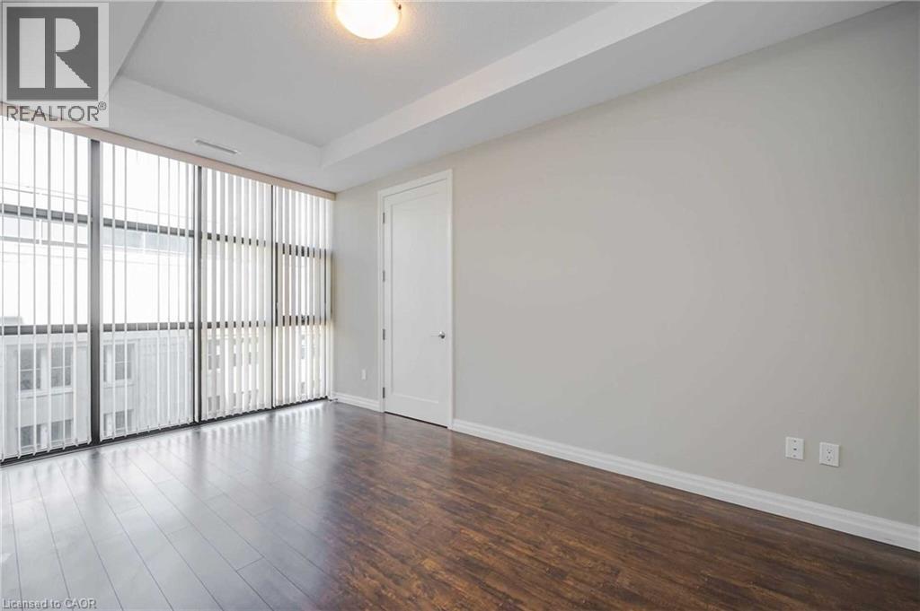 Expansive window wall with vertical blinds, wood-finish flooring, crisp white baseboards, a single panel interior door, and a tray ceiling - 112 King Street E Unit# 907, Hamilton, ON