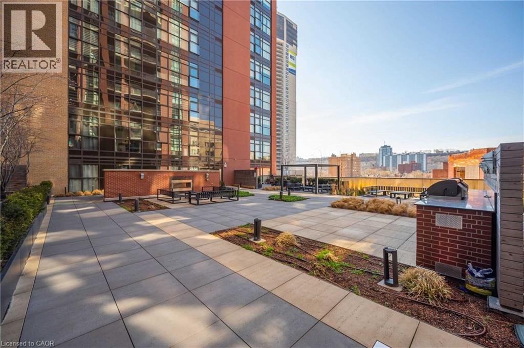 Expansive rooftop patio featuring a paver surface, integrated planter beds, and a built-in brick barbecue station with a countertop - 112 King Street E Unit# 907, Hamilton, ON