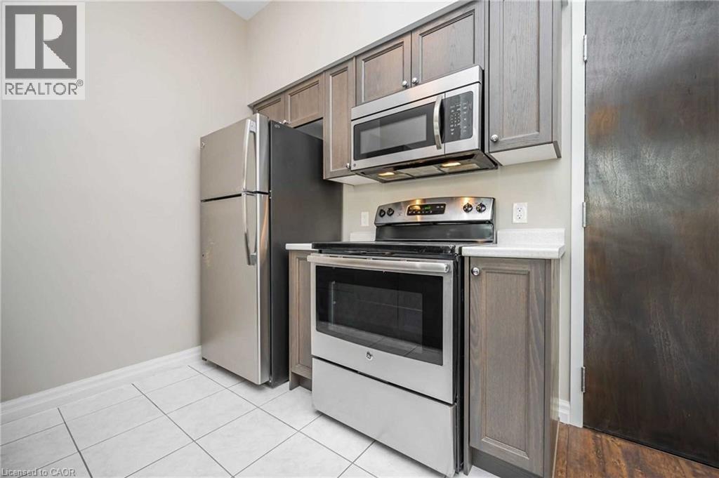Kitchen featuring stainless steel appliances, grey wood-finish cabinetry, white countertops, and white tile flooring - 112 King Street E Unit# 907, Hamilton, ON