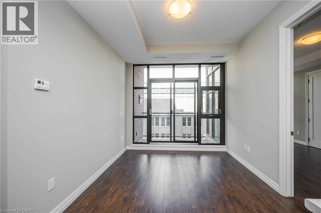 Expansive window wall with sliding glass door, dark wood-finish flooring, light grey painted walls, white baseboards, and a recessed ceiling feature - 112 King Street E Unit# 907, Hamilton, ON