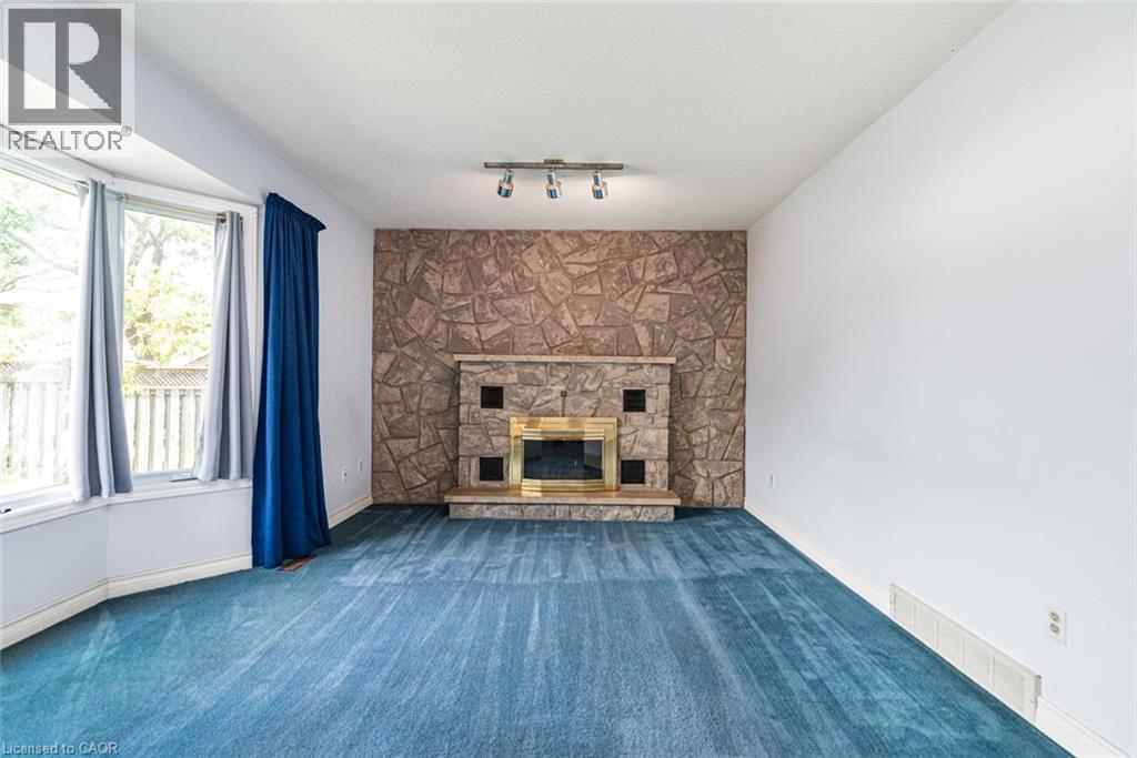 Spacious room featuring a stone-clad fireplace with a brass-trimmed insert, blue carpeting, and a bay window - 381 Kerman Avenue, Grimsby, ON - Indoor With Fireplace