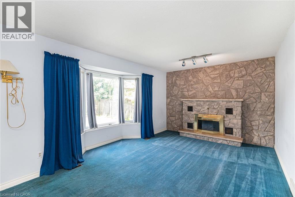 Living area featuring a stone accent wall with a built-in fireplace, a bay window, track lighting, and wall-to-wall carpeting - 381 Kerman Avenue, Grimsby, ON - Indoor Photo Showing Other Room With Fireplace