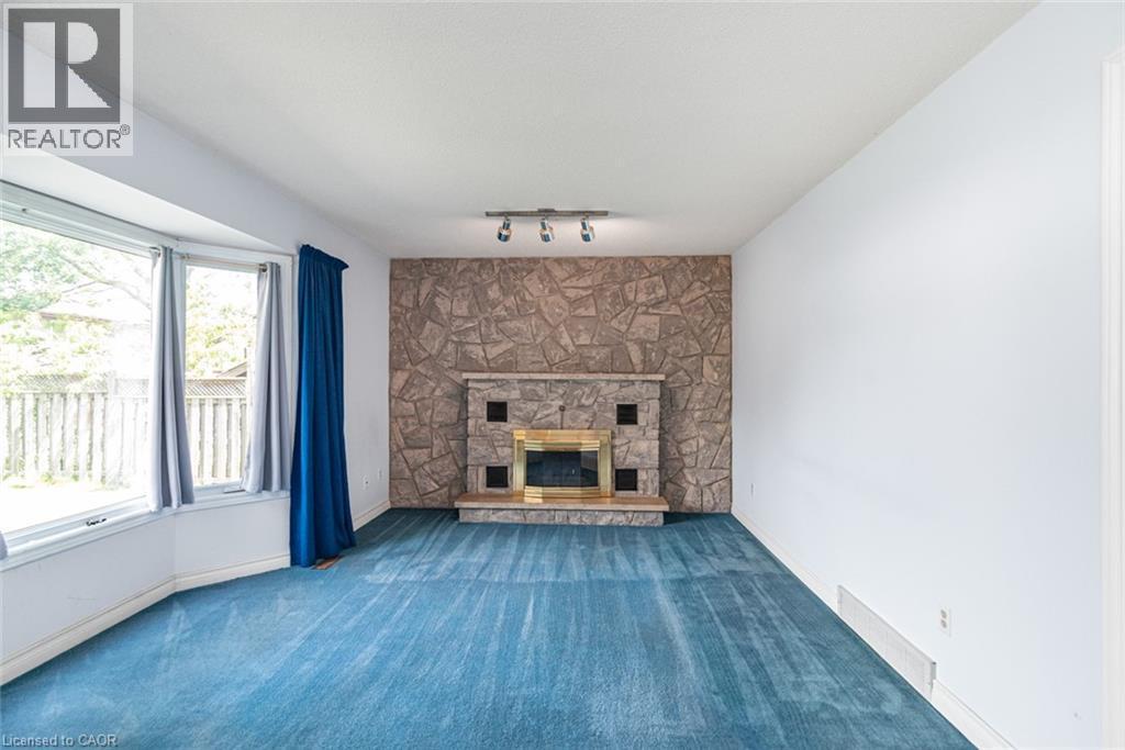 Living area featuring a stone accent wall with an integrated fireplace and brass trim - 381 Kerman Avenue, Grimsby, ON - Indoor Photo Showing Living Room With Fireplace