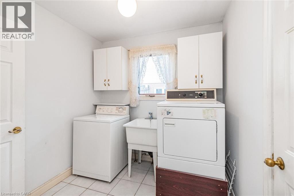 Laundry room featuring a utility sink, white wall-mounted cabinetry, white tile flooring, and a window for natural light - 381 Kerman Avenue, Grimsby, ON - Indoor Photo Showing Laundry Room