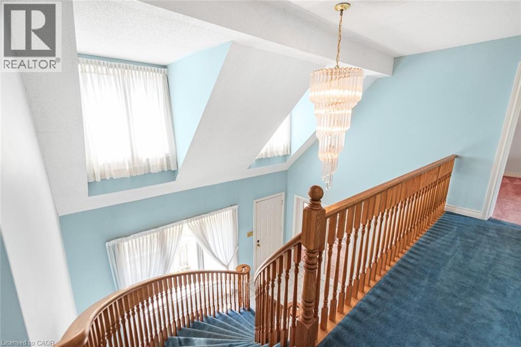 Staircase featuring a wood-finish handrail and balusters, a tiered crystal chandelier, and a curved design - 381 Kerman Avenue, Grimsby, ON - Indoor Photo Showing Other Room