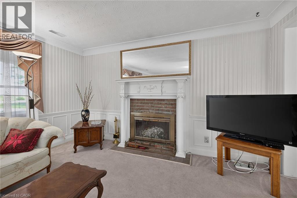 Formal living area featuring a brick fireplace with a white mantel, textured wallpaper, crown molding, and wainscoting - 114 E Second Road E, Stoney Creek, ON