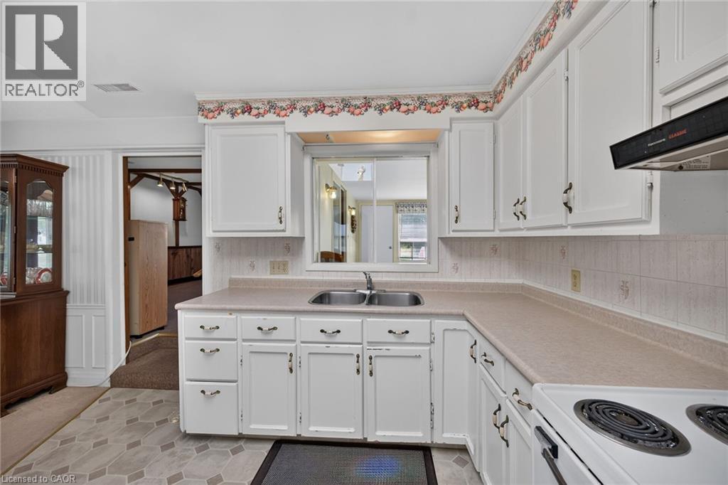 Kitchen featuring white cabinetry, a double basin stainless steel sink, and a four-burner electric range with an overhead vent - 114 E Second Road E, Stoney Creek, ON