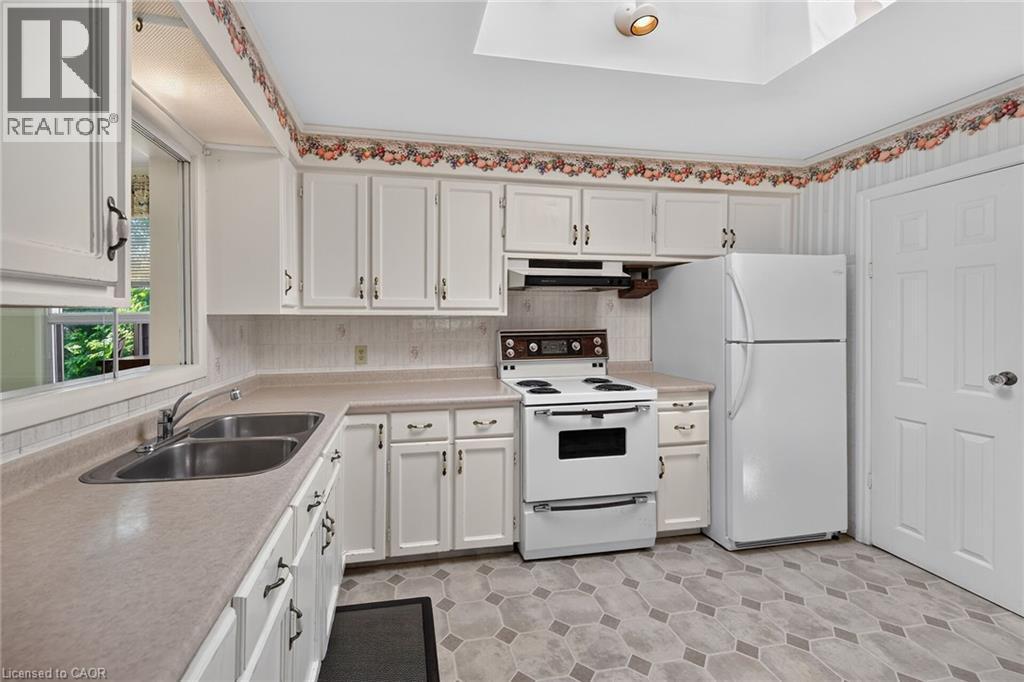 Kitchen featuring white cabinetry, a double basin stainless steel sink, and a light-toned countertop - 114 E Second Road E, Stoney Creek, ON