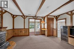 Expansive living area featuring exposed wood beams, wood-panel wainscoting, and a brick fireplace with a black cast iron stove -