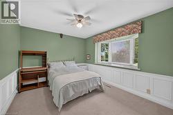Bedroom featuring a bay window, wainscoting, ceiling fan with integrated lighting, and carpet flooring -