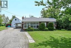 Brick exterior with a large front lawn, mature trees, an attached carport, and a separate barn structure -