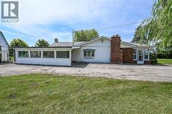 White siding exterior with a prominent brick chimney and a large paved area -