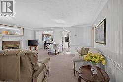 Living area featuring a brick fireplace with a white mantel, textured white wallpaper, light-colored carpeting, and crown molding -