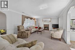 Living area featuring a fireplace with a stone surround and ornate mantel, light-colored carpeting, wainscoting, striped wallpaper, and an arched doorway -