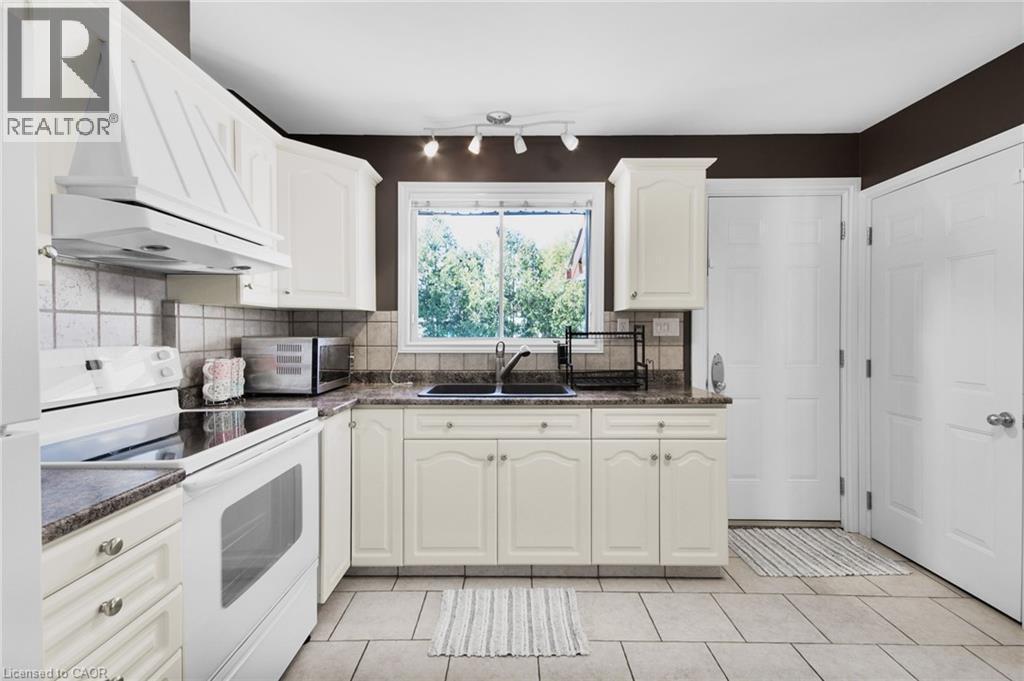 Kitchen featuring cream-colored cabinetry, tile flooring, granite-style countertops, a double basin sink, and a window with exterior visibility - 185 Burlington Street, London, ON
