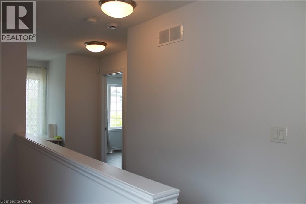 Upper-level hallway with white painted walls and trim, featuring a window with patterned sheers and two flush-mount ceiling lights - 27 Stillwater Street, Kitchener, ON