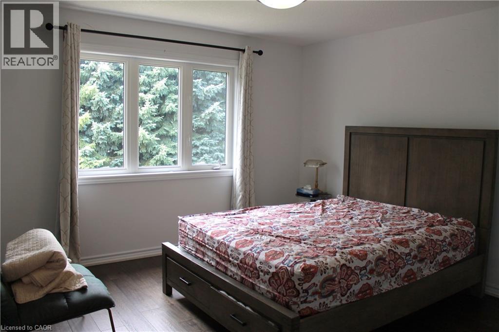 Bright bedroom featuring white walls, wood-finish flooring, a three-panel window, and white trim - 27 Stillwater Street, Kitchener, ON