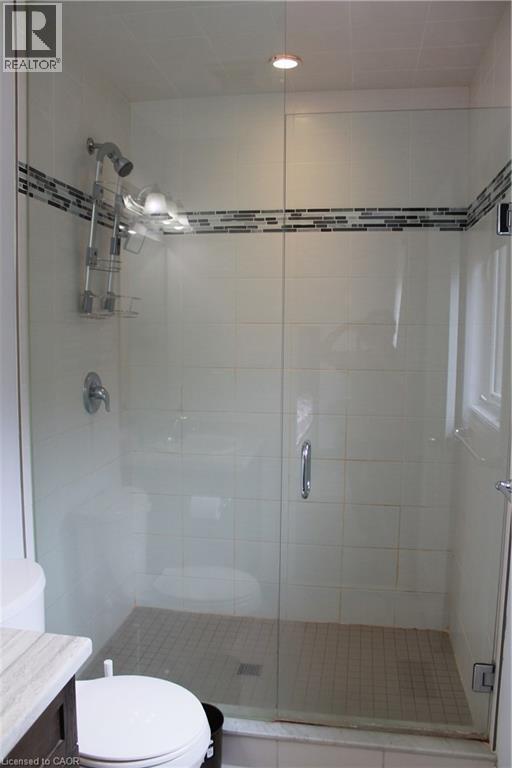 Glass-enclosed shower featuring white ceramic wall tiles with a decorative mosaic accent strip - 27 Stillwater Street, Kitchener, ON