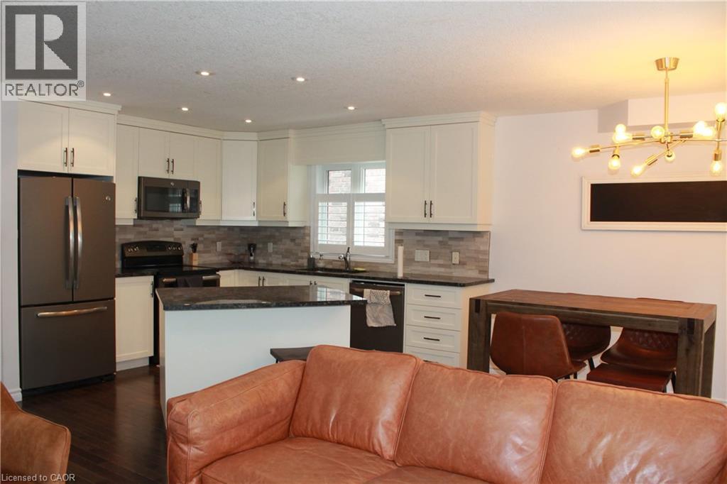 Open-concept kitchen featuring white cabinetry, dark stone countertops, a tile backsplash, and stainless steel appliances - 27 Stillwater Street, Kitchener, ON